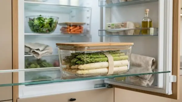 Frischer Spargel neben offenem Kühlschrank zur richtigen Lagerung